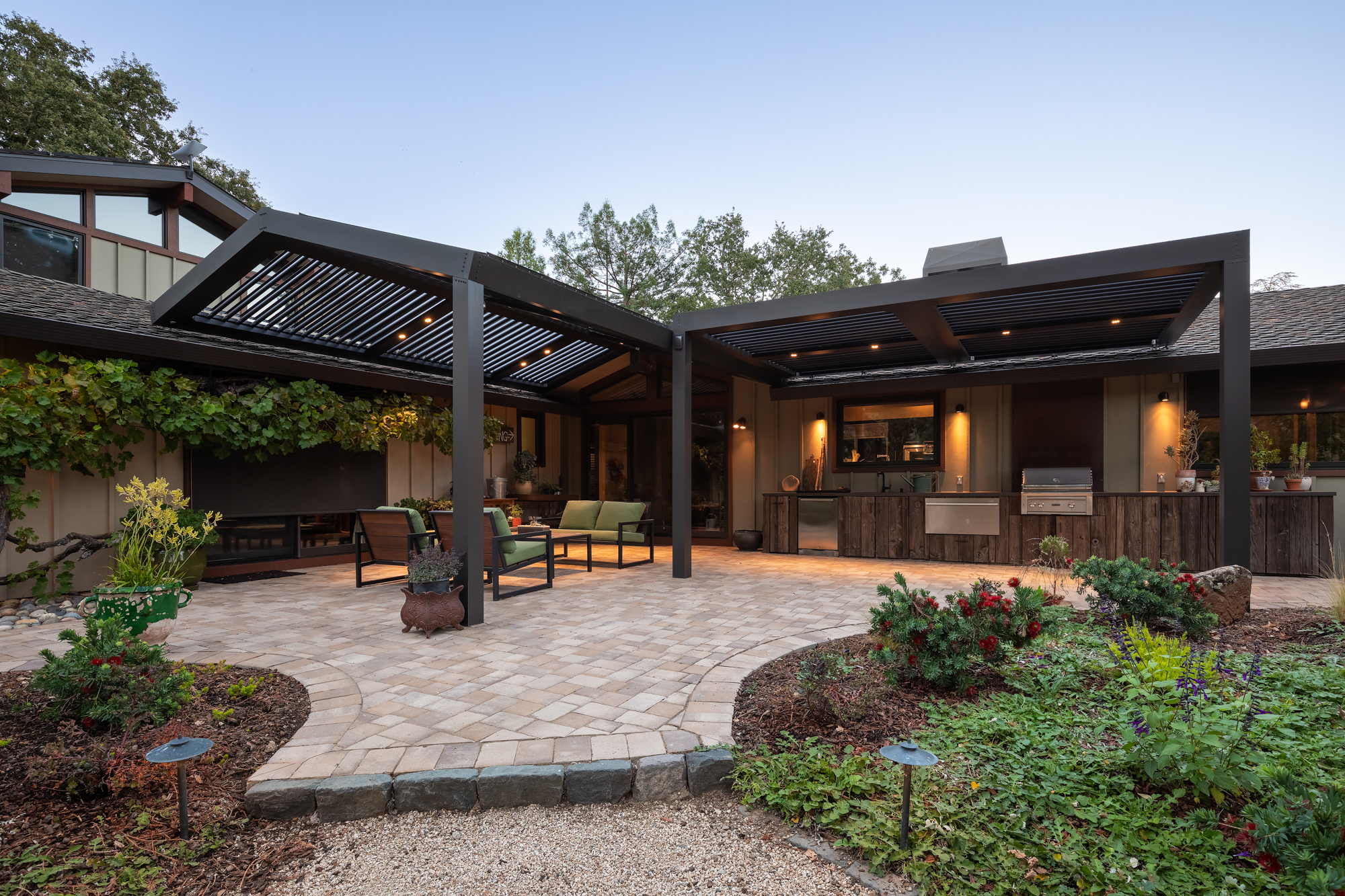 Interior view of dark aluminum louvers partially open over an outdoor living space.
