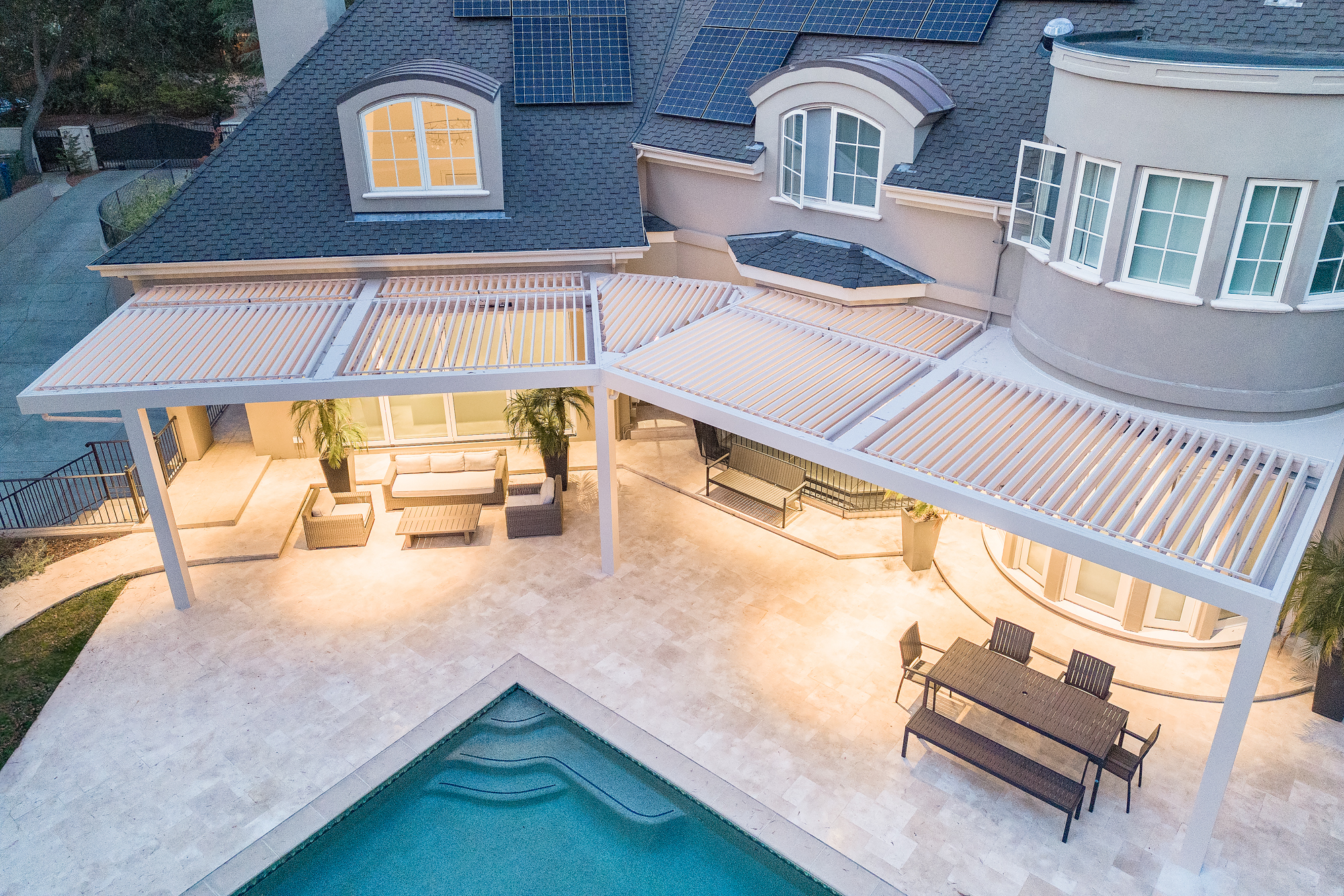 Aerial view of an L-shaped motorized pergola system spanning the rear of a luxury estate.