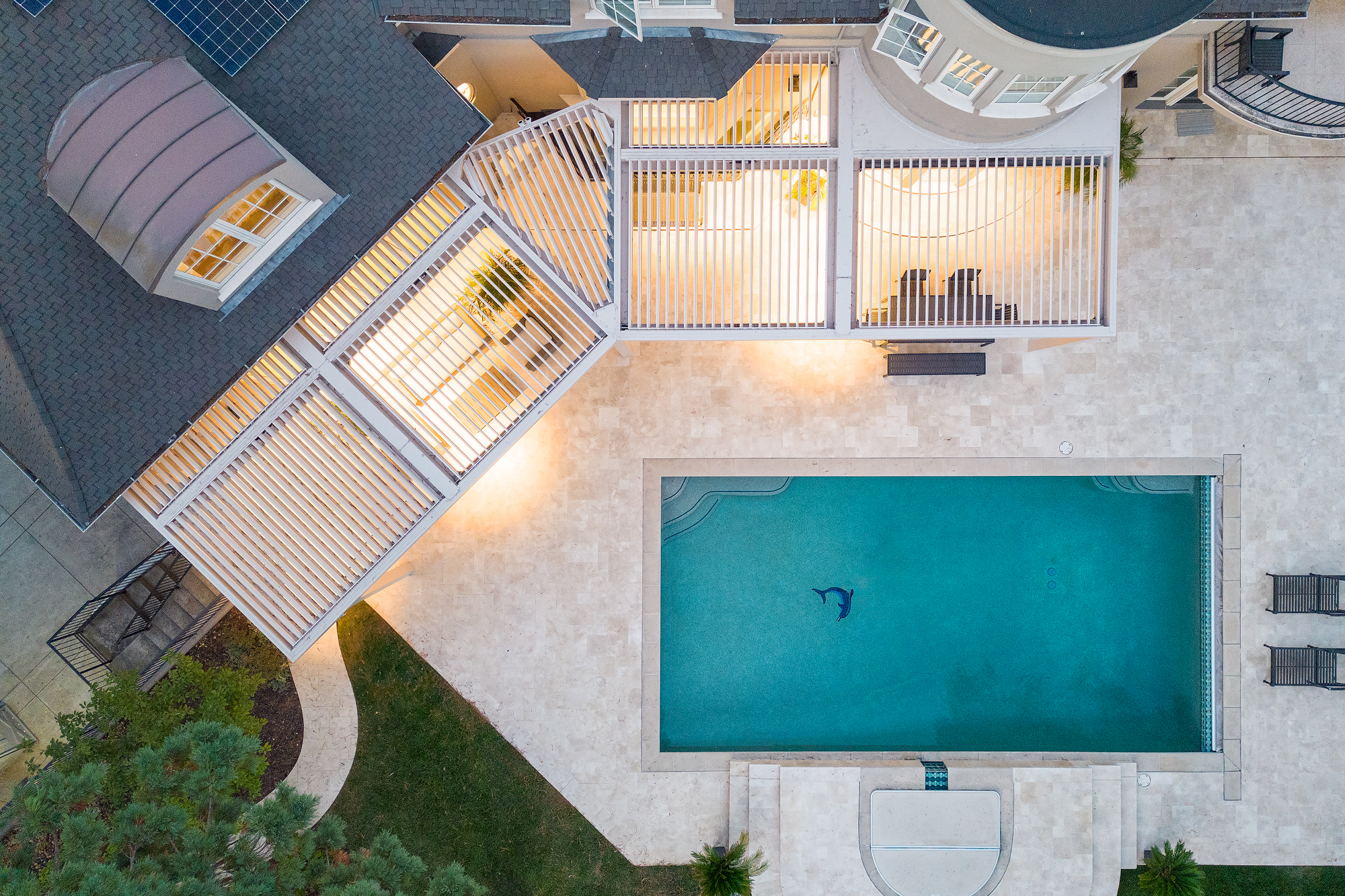 Drone overhead shot of a poolside pergola lit from below at twilight.